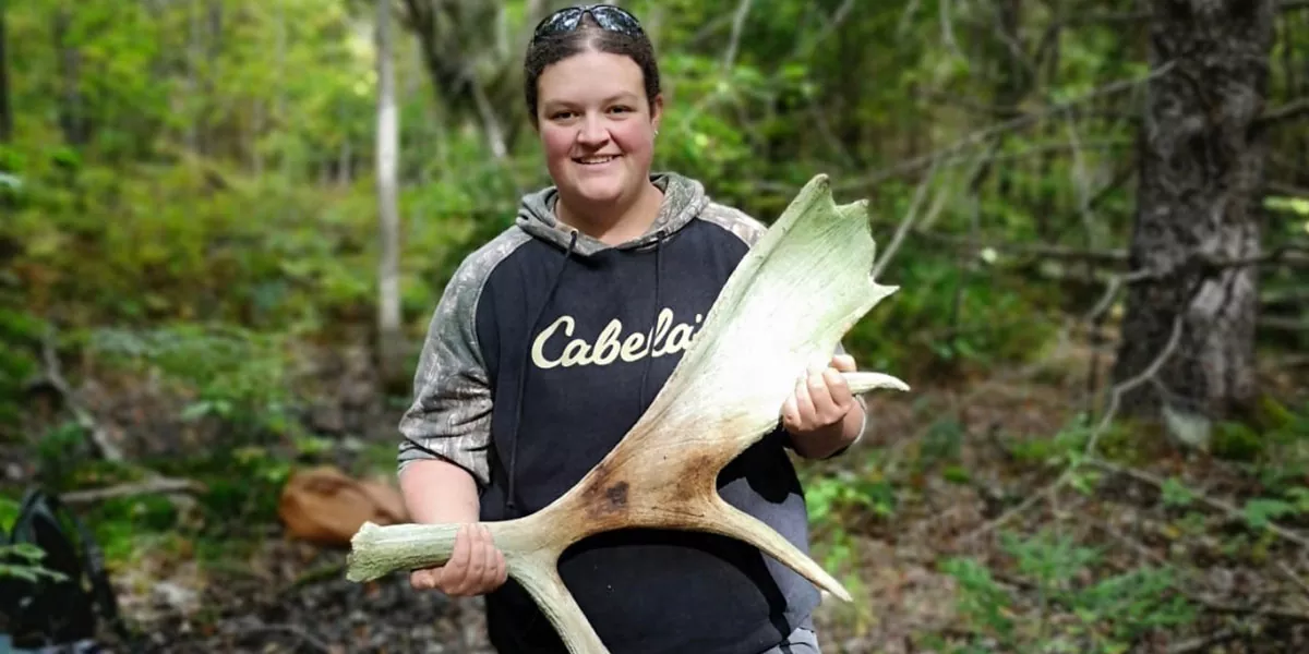 Calli standing in a forest holding a moose antler