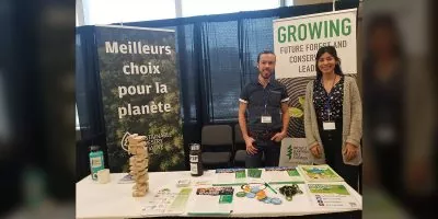 Maria standing with Paul behind PLT Canada table at event