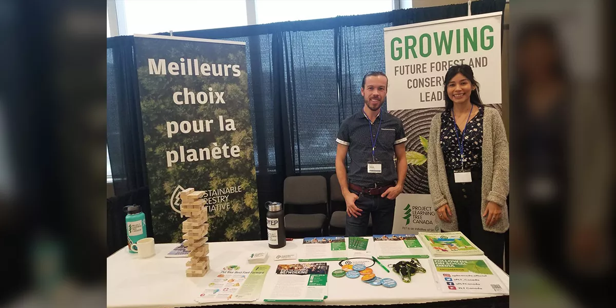 Maria standing with Paul behind PLT Canada table at event