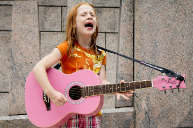 Young girl sings while playing a pink guitar