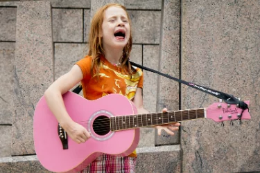 Jeune fille chante en jouant une guitare rose