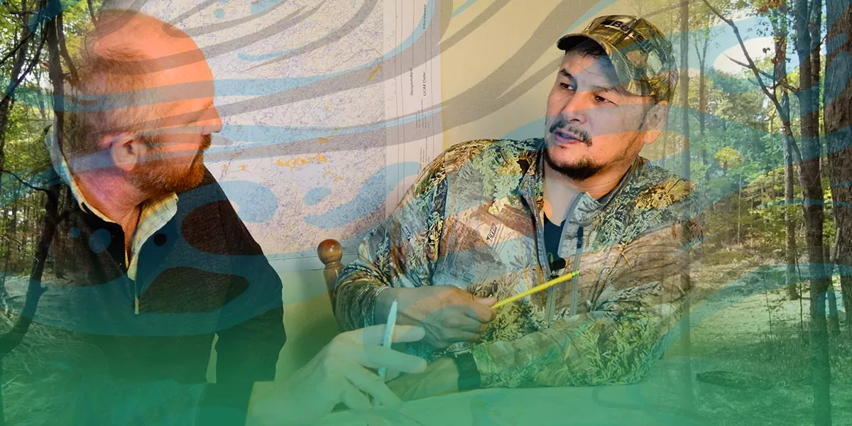 An Indigenous man in camouflage clothing talks to a Caucasian man in an office