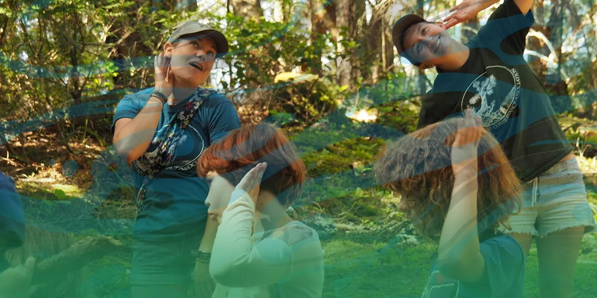A young woman (environmental educator) playing with children in a wooded area.