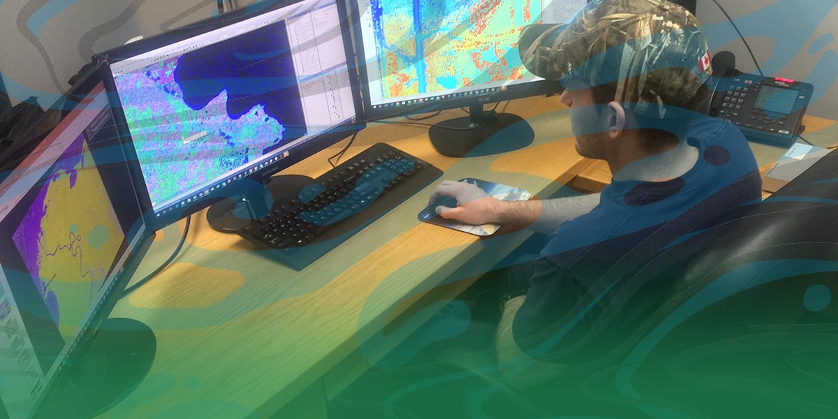 A man (GIS technician) sits in front of 3 computer monitors showing area maps.