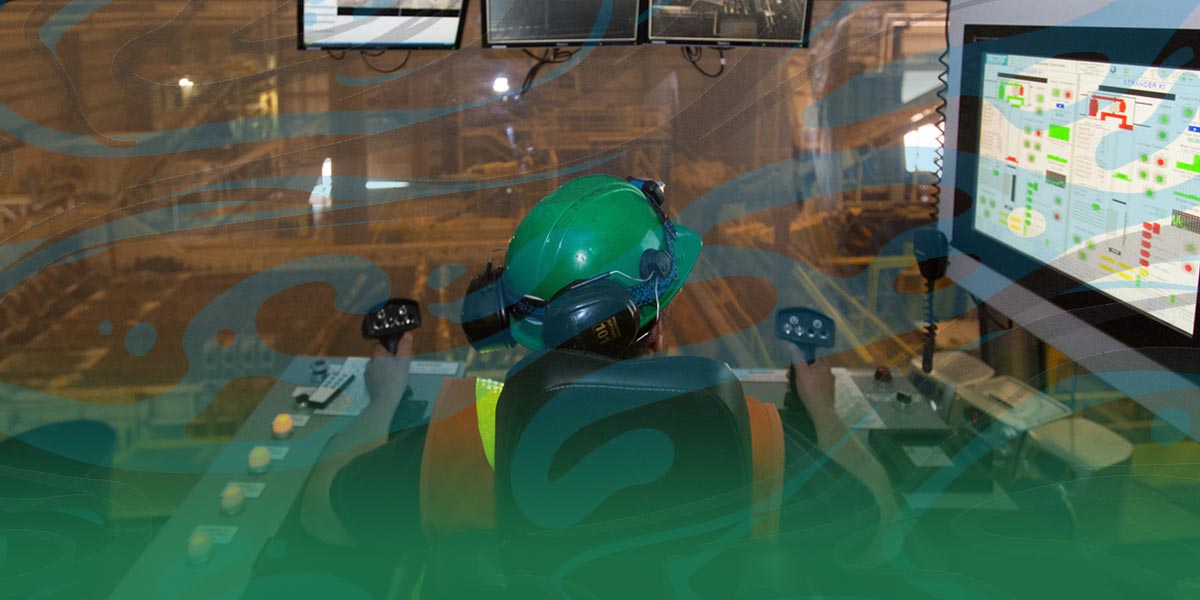 A machine operator operates complicated looking equipment in front of 4 display monitors.