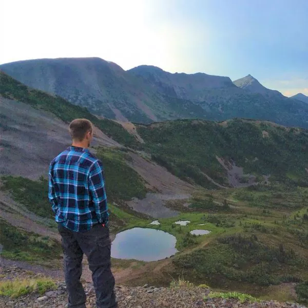 young man on hilltop looks out over forested landscape below