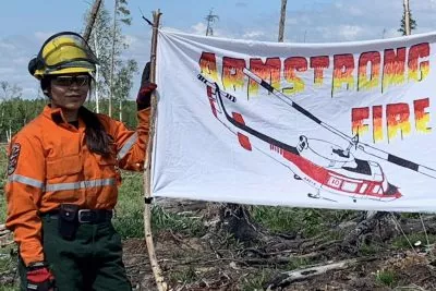 A young person in firefighting gear holds an Armstrong Fire flag