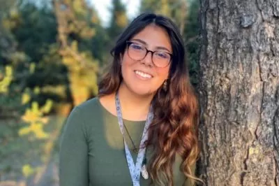 A young woman leans against a tree, smiling