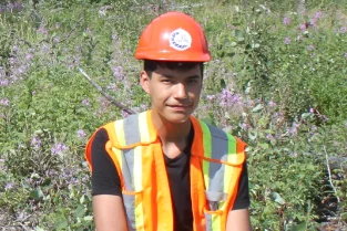 A young person sitting in the forest, wearing a vest and hard hat