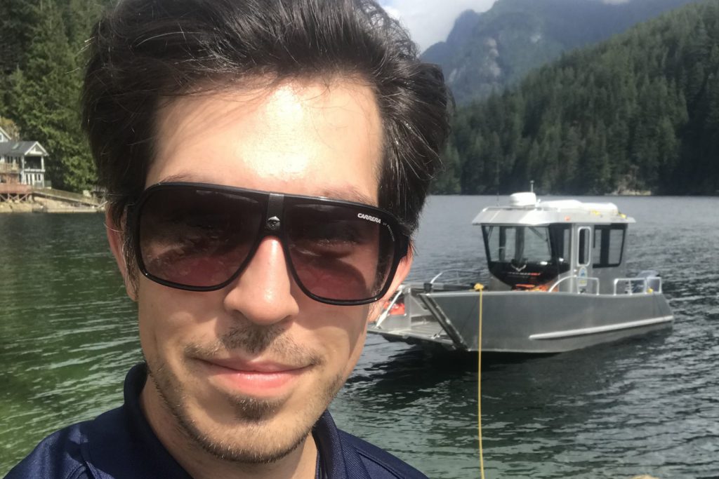 A young person takes a selfie in front of the water and mountains