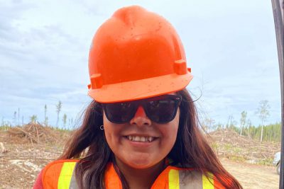 smiles, wearing a hard hat, sunglasses and vest