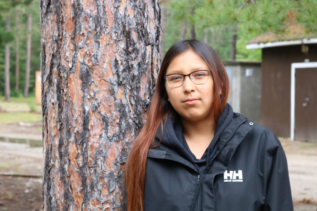 A young person leans on a tree