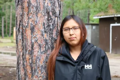 A young person leans on a tree