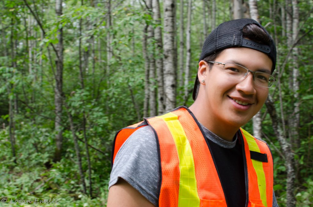 A young person smiling in the forest, wearing a vest