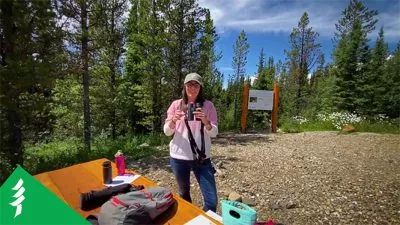 Laura holds a pair of binoculars, next to an outdoor table covered in her supplies