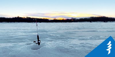 A fishing rod standing upright next to a hole in the ice.