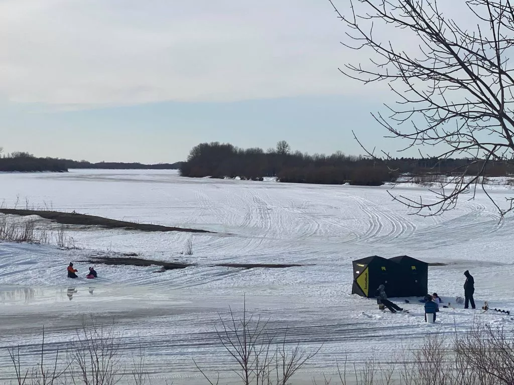 A family sitting around an ice fishing hole, next to an ice fishing tent