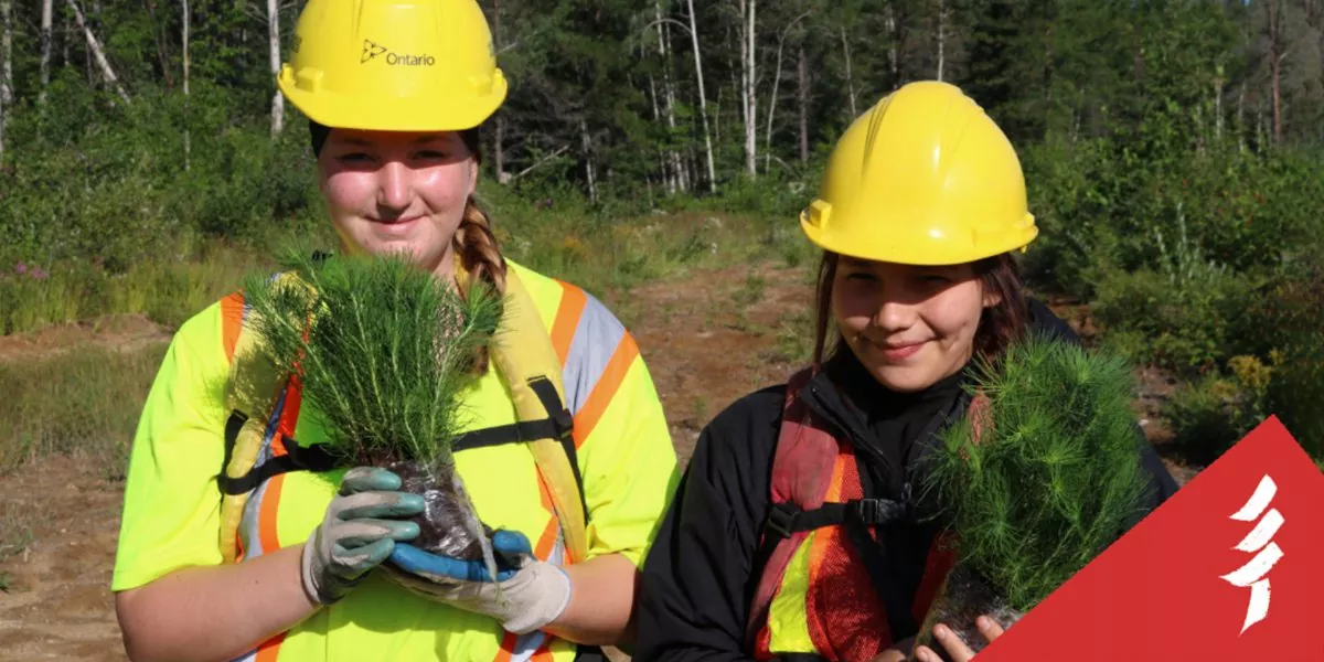 Two youth in hard hats holding baby trees.