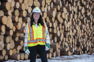 Amy Rose stands in front of logs, wearing a hard hat and vest