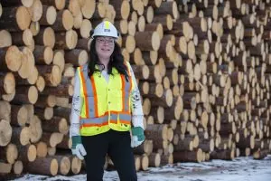 Amy Rose stands in front of logs, wearing a hard hat and vest