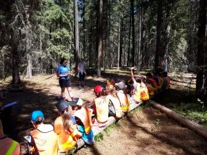 Young people sit on a log in a forest and listen to an educator