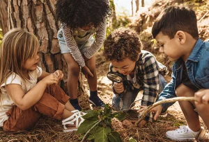 Four young children gathered around a lead, inspecting it with a magnifying glass
