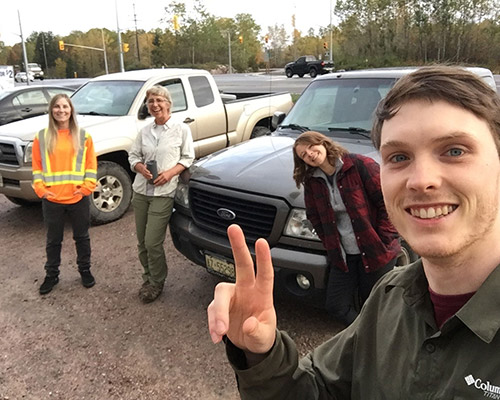 three women and a young man stand in a parking lot with some pick up trucks