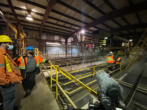 Several men in orange protective clothing look out over operations inside a forestry mill.