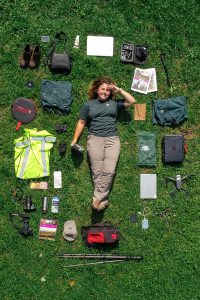 A young woman lies down in the grass, surrounded by her work equipment