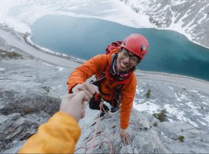 Someone reaches out their hand to help a young man climbing mountain
