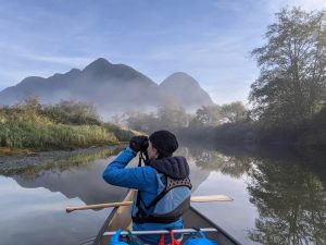 A young woman in a canoe looks out of binoculars