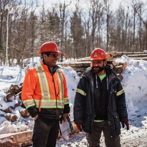 2 men in hard hats stand in front of a forest