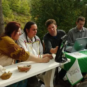 Four people sitting at a desk with computers, in the forest