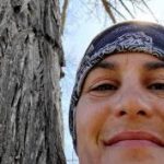 Jeanette smiles at the camera beside a tall tree