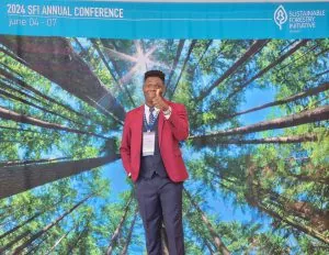 Mayowa giving a thumbs up in front of the conference banner.