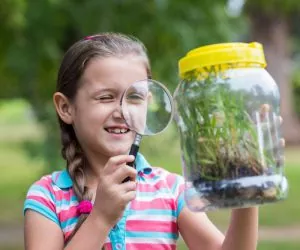 Little girl looking at a jar with a magnifying glass